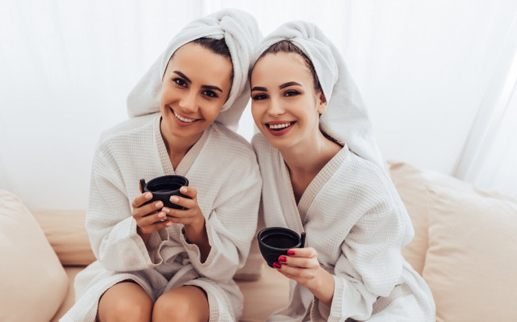 dwie przyjaciółki w szlafrokach i z ręcznikami na włosach piją herbatę w spa